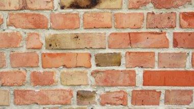 Kırmızı ve turuncu renkli eski tuğla duvar - soyut arkaplan kompozisyonu. Tuğla delikleri ve aşınmalarla kaplanmış. 4k 25FPS içerisindeki eski hasarlı duvar iskeleti yüzeyi hakkında video görüntüleri