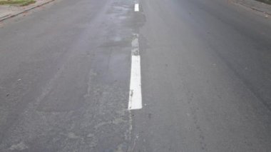 Gri asfalt yolu, beyaz şeritli. Eski yoldaki hasarları zaman içinde ayırın. Kaldırımlı ve yanında sarı yapraklar olan arabalar için boş bir yol. HD 25FPS 'te video görüntüleri