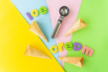 Waffle külahı ve metal dondurma kaşığıyla düz kompozisyon, farklı parlak arkaplanlarda yazılı dondurma.