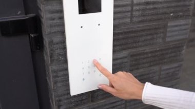 Beyaz bir kadın elektronik bir kapı panelindeki daire kodunu çeviriyor. Kız, elektronik bir dahili telefonun beyaz, modern kapı telefon panelinden numarayı çeviriyor. Koruma ve güvenlik kavramı