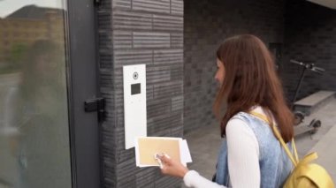 Anahtarları, mektupları ve sırt çantasıyla genç esmer kadın dahili telefondan arama kodunu çeviriyor. Genç kız el sallıyor ve elektronik kilidin kamerasına bakıyor. Kapıdaki kız.