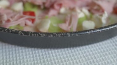 Lezzetli peynir, jambon, pırasa ve vişneli domatesli taze çiğ pizza yakın çekim. Gri-siyah tabakta pişmeye hazır lezzetli İtalyan pizzası manzarası. 4K 25FPS 'de yiyecek ve içecek video görüntüleri.