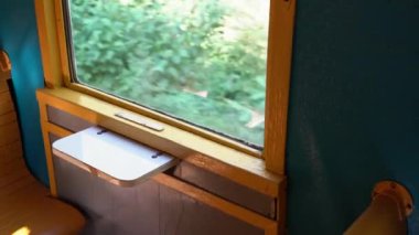 Hareket halindeki eski bir vagonun penceresinden görüntü. Eski bir tren, güneşli bir günde ormanda yavaşça yol alır ve boş bir vagonun ahşap penceresinden titreyen ağaçları görebilir. Tren yolculuğu.