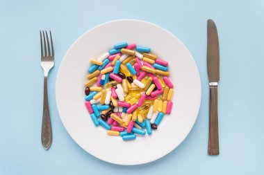 Birçok çok renkli parlak vitaminler bıçak ve çatalla birlikte bir tabakta yatar. Sağlık hizmeti, sağlıklı beslenme, diyet