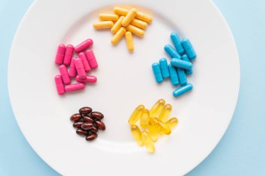Parlak renkli besin maddeleri mavi arka planda beyaz bir tabakta yatar. Sağlık desteği ve vitamin eksikliği kavramı