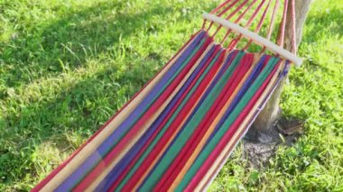 Güneşli bir yaz gününde gün batımında tropik plajda rüzgarda sallanan boş renkli hamak. Yeşil bir bahçede çizgili bir hamak asılı duruyor. Açık hava eğlencesi, hafta sonu parkta 4K 'da.