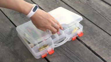 Kadın elinde farklı renkte balık bujileriyle dolu plastik kabı açıyor ve bir krank-bait 'i yakından çekiyor. Balık tutmaya hazırlanırken tahta iskelede balık yemi taşıyan kız eli.