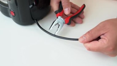 Adam penseyi elinde tutuyor ve elektrik kablosunu ısırıyor. Eller, tamir ustası ve elektrikli teli kesen meme uçlarına yakın çekim. Enerji tasarrufu, güç kısıtlaması ve elektrik kesintisi kavramı