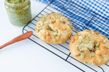 Ayçiçeği tohumlu yeni pişmiş bir simit, metal bir standın üzerinde kareli bir peçete ve ahşap bir bıçakla birlikte yatıyor.