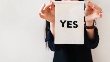 Siyah takım elbiseli genç bir iş kadını beyaz izole bir arka planda beyaz bir ilan panosu gösteriyor. Posterde evet yazıyor. İş ve reklam kavramı. Pankart