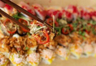 Bir el sanatları kutusunda suşi ruloları, ahşap çubuklarla bir parça tutan eller. Paket, paket.