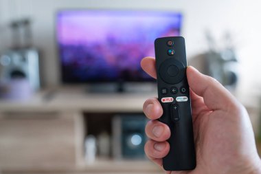 Bir kadının elinde Netflix 'e, Prime Video kanallarına hızlı bağlanmak için düğmeler bulunan uzaktan kumanda var. Çalışma gününden sonra dinlenin.