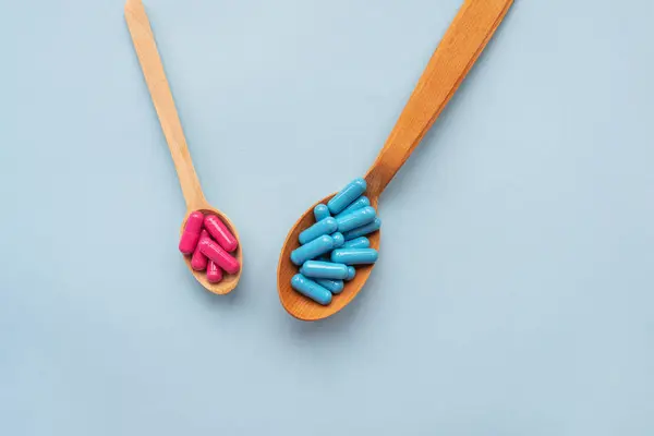 Vitamins of bright colors in wooden spoons on a blue background. Pharmaceutical industry. Healthcare and medicine. Pharmacy product