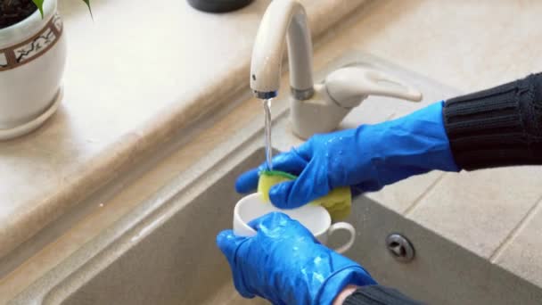 若い女性の汚れたビデオは 自宅で掃除をしている間にスポンジを使ってコーヒーカップを洗っています 青いゴム製手袋の主婦の手のクローズアップキッチンシンクで皿を洗う 4K映像 25Fps — ストック動画