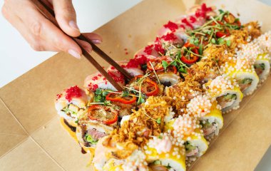 El sanatları kutusunda farklı tipte suşi ruloları, bir kızın eli tahta çubuklarla bir parça tutuyor. Paket, paket.