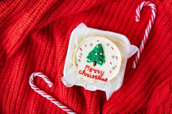 一个节日的圣诞纸杯蛋糕 顶部有白霜和绿树 背景是红色针织的糖果手杖 圣诞贺信 — 图库照片#