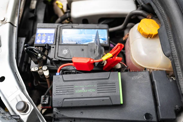 car engine with a diagnostic tool attached. The tool is a small black box with a red and black wire attached to it. The tool is connected to the car battery and the engine