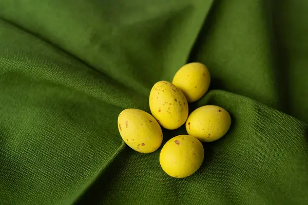 Five yellow speckled eggs on a folded green fabric with woven texture. Eggs with small brown spots, the combination of yellow eggs and green tissue creates a striking contrast