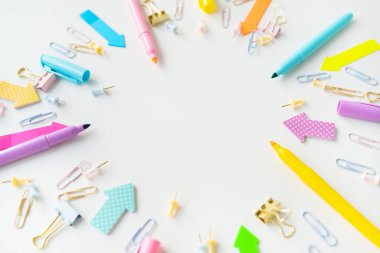 Colorful assortment of office supplies including pens, markers, paper clips and paper clips scattered on a white background. The overall mood is bright and creative, with space for writing