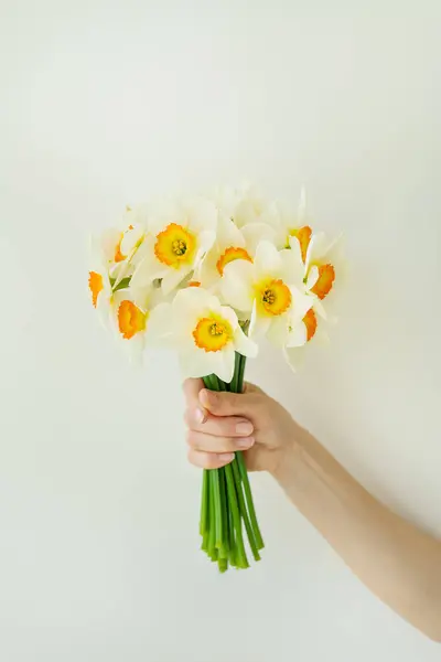 Hand bouquet of fresh daffodils on a plain white background. The green stems of the flowers are neatly tied together and held tightly in the hand