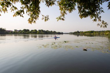 Huzurlu bir göl manzarası, sakin suların ortasında kayak yapan bir insan. Görüntü, açık hava eğlencesi, eğlence ve refahı için idealdir.
