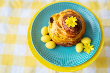 Sarı çiçekler ve şekerlemelerle süslenmiş mavi bir tabakta nefis hamur işleri, kareli masa örtüsü üzerinde. Paskalya tatili konsepti