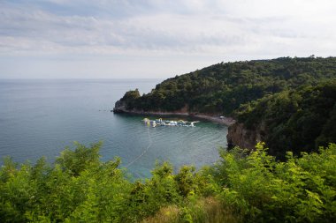 Deniz kenarında bulutlu bir gökyüzünün altında şişme bir su parkı olan sakin bir sahil manzarası.
