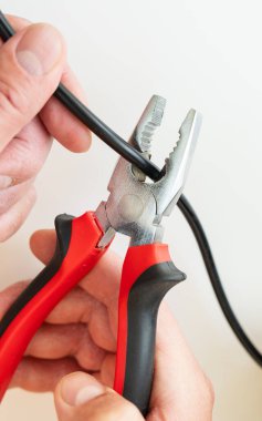 Siyah kabloyu kesmek için kerpeten kullanan ellerin yakın çekimi, DIY elektrik onarım görevi