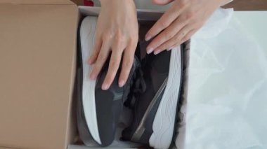 Bir kadın yeni siyah beyaz spor ayakkabıları açıyor ve onları yakından inceliyor..