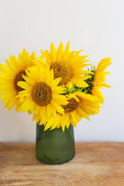 Kaburgalı yeşil bir vazoda canlı ayçiçekleri kırsal bir ahşap masayı parlatır..