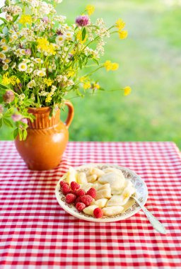 Kırsal bir yaz sofrasında, kil bir sürahide bir buket yabani çiçekle tamamlanmış ahududu ile bir tabak hamur köftesi bulunur..