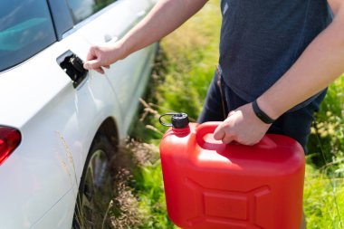 Adam yol kenarındaki beyaz arabasına kırmızı bir teneke kutudan yakıt ekliyor..
