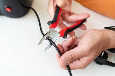 Bir insan elektrik kablosunu kesmek için dikkatlice kerpeten kullanır. Elektrik işine ya da tamirine hazırlanır..