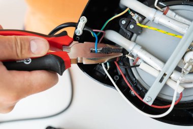 Bir insan elektrikli su ısıtıcısının iç kablolarını tamir etmek için pense kullanır..