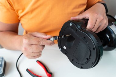 Bozuk bir aleti dikkatlice tamir eden kişi küçük bir tornavida kullanarak DIY ev onarımını gösteriyor..