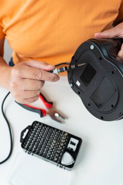 Bir kişi bozuk bir aleti titizlikle küçük bir tornavida ve bir takım aletler kullanarak tamir eder..