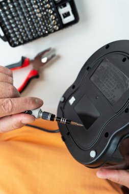 Bir kişi, küçük bir tornavida ve diğer aletlerle bozuk bir aleti dikkatlice tamir eder ve tamir işleminin detaylı bir yakın çekimini gösterir..