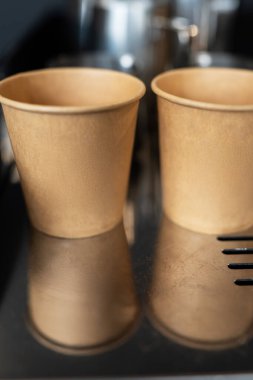 Baykuş logosuna sahip iki boş kağıt kahve fincanı metalik bir yüzeyde oturuyor ve basit ama şık bir kafe markası sergiliyor..