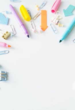 Kalemler, ataçlar ve raptiyeler gibi pastel renkli kırtasiye ürünleri beyaz bir arkaplanda düzenlenerek neşeli ve düzenli bir çalışma alanı oluşturulur..