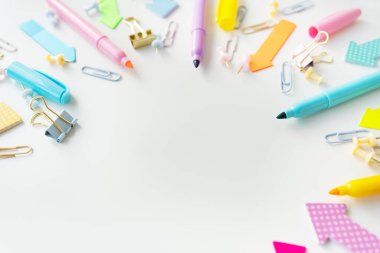 Kalemler, ataçlar ve raptiyeler de dahil olmak üzere renkli kırtasiye ürünleri, beyaz arkaplanda sanatsal bir şekilde düzenlenmiş, canlı ve eğlenceli bir sahne yaratıyor.