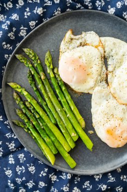 Lezzetli ve sağlıklı bir kahvaltı. Koyu gri tabakta servis edilen kızarmış sarımsaklı yumurta ve kuşkonmaz..