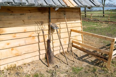 Yaba, kürek, tırmık ve süpürge de dahil olmak üzere eski tarım aletleri, kırsal bir ahşap kulübeye yaslanıyor..