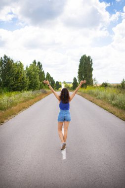Çekici kız, poz veriyor, ellerini kaldırıyor, alanın yakınındaki asfalt yolun ortasında, içerik alanı kopyalıyor.