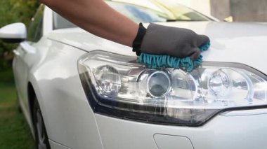 Araba tamiri. Koruyucu eldiven, mikrofiber bezle beyaz bir arabanın farlarını siler. Otomatik bakım, temizlik servisi.