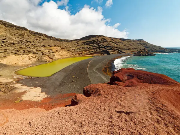 Lanzarote 'nin volkanik manzarasının güzelliği. Zümrüt yeşili göl, Charco de los Clicos, adanın eşsiz jeolojisinin çarpıcı bir örneğidir. Etrafındaki kırmızı kayalıklar, siyah kum ve sarı kayalar dramatik ve renkli bir ortam yaratır..