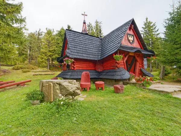 Tepenin tepesinde kırmızı çatılı ahşap bir ev.