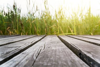 Göl kıyısındaki ahşap yol. Yeşil çimenler ve günbatımı arka planı.