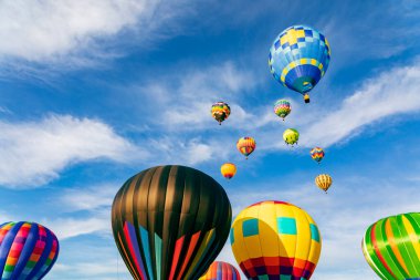Mavi gökyüzünde beyaz bulutlarla uçan renkli sıcak hava balonları