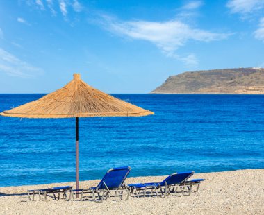 Summer morning pebbly beach with sunbeds and strawy sunshade (Borsh, Albania).