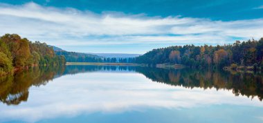 Autumn misty evening lake panorama with grove on shore.